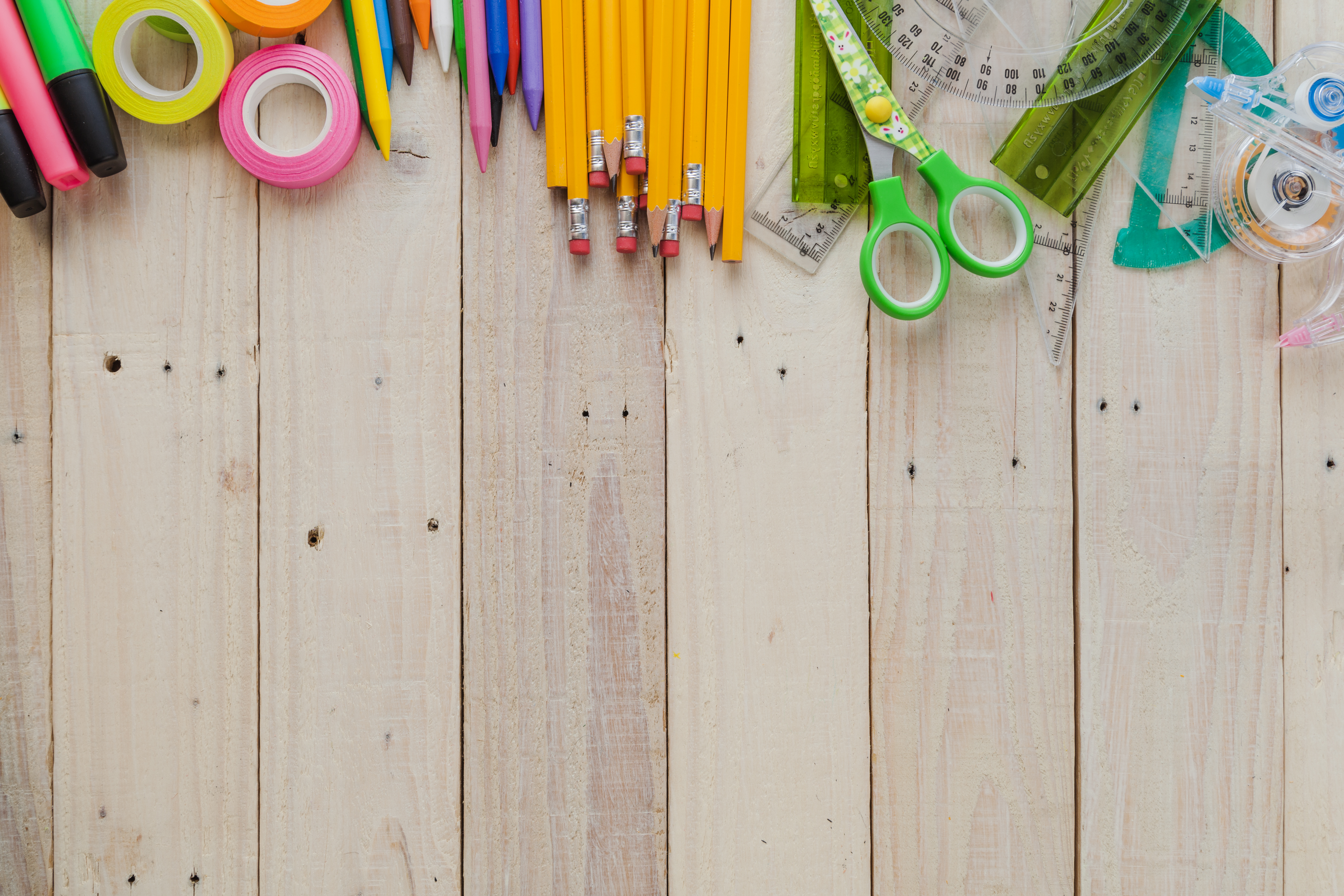 Various craft supplies including pencils, scissors, and tape on a wooden plank background.