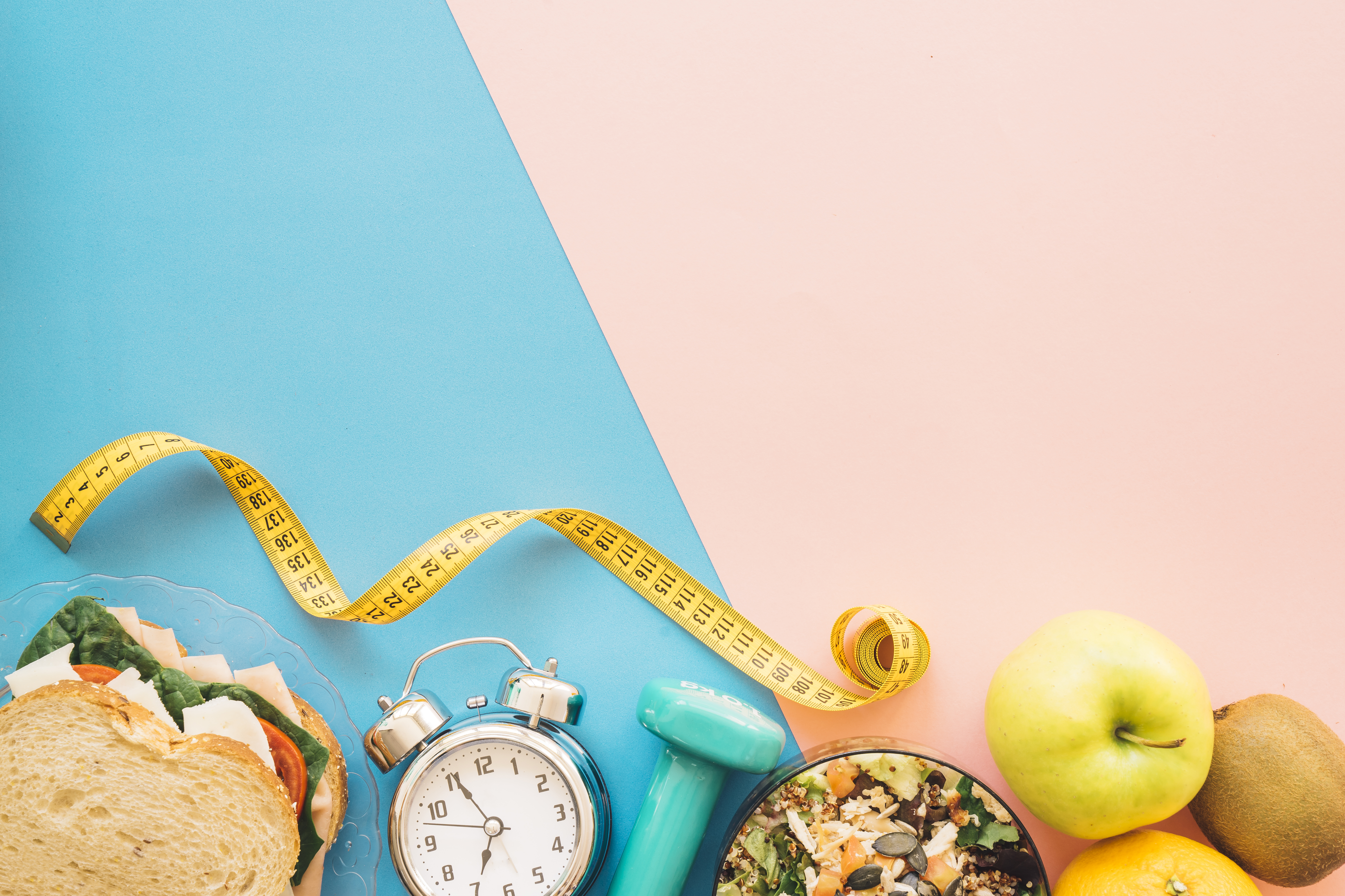 A sandwich, alarm clock, small weight, tape measure, and fruit on a blue and pink background.