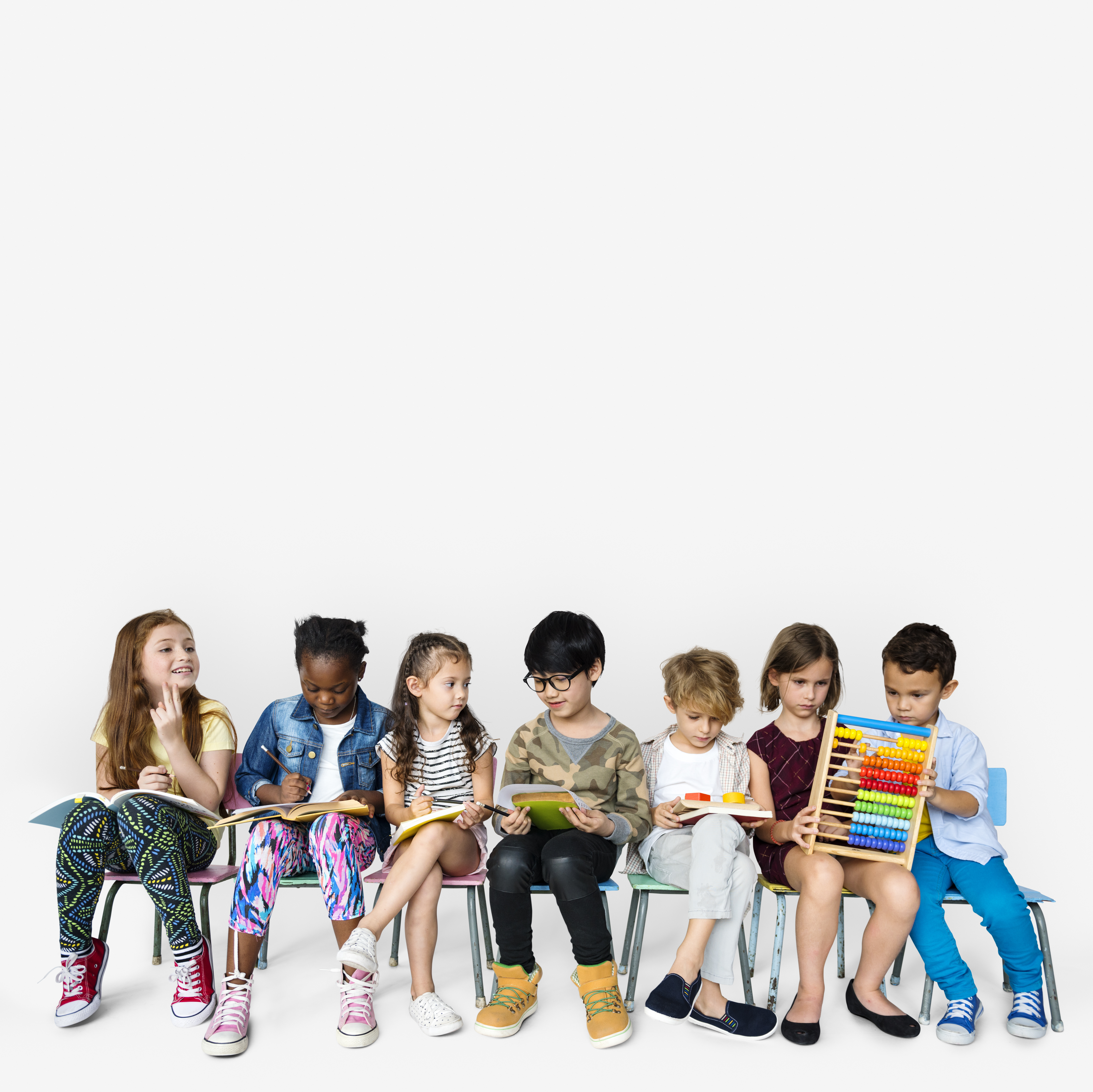 Group of kids sitting in chairs holding books, pencils, and an abacus on a white background. 