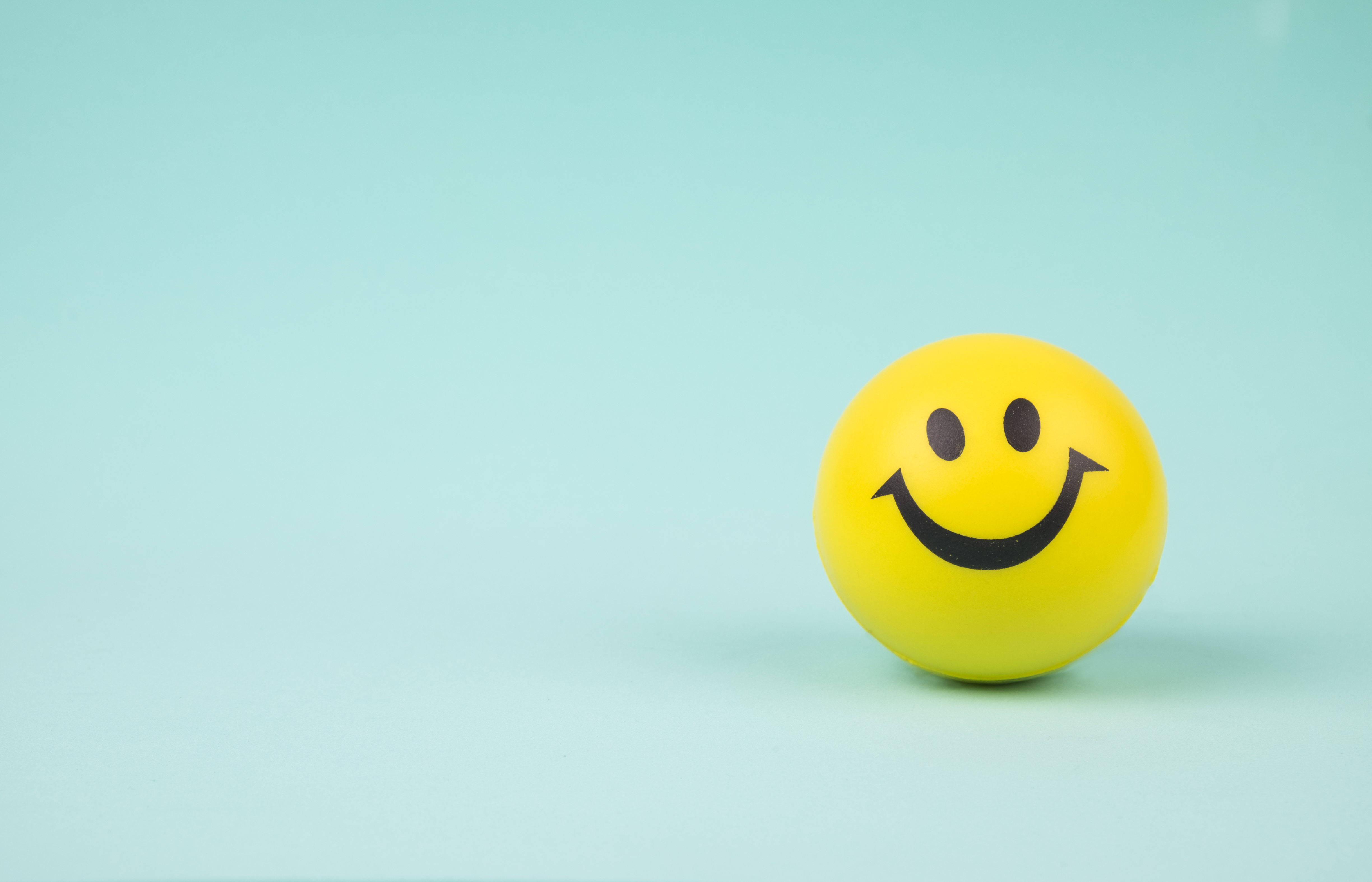 Yellow smiley face stress ball on an ocean blue background.