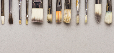 Various paintbrushes lined up along top of photo. The background is beige.