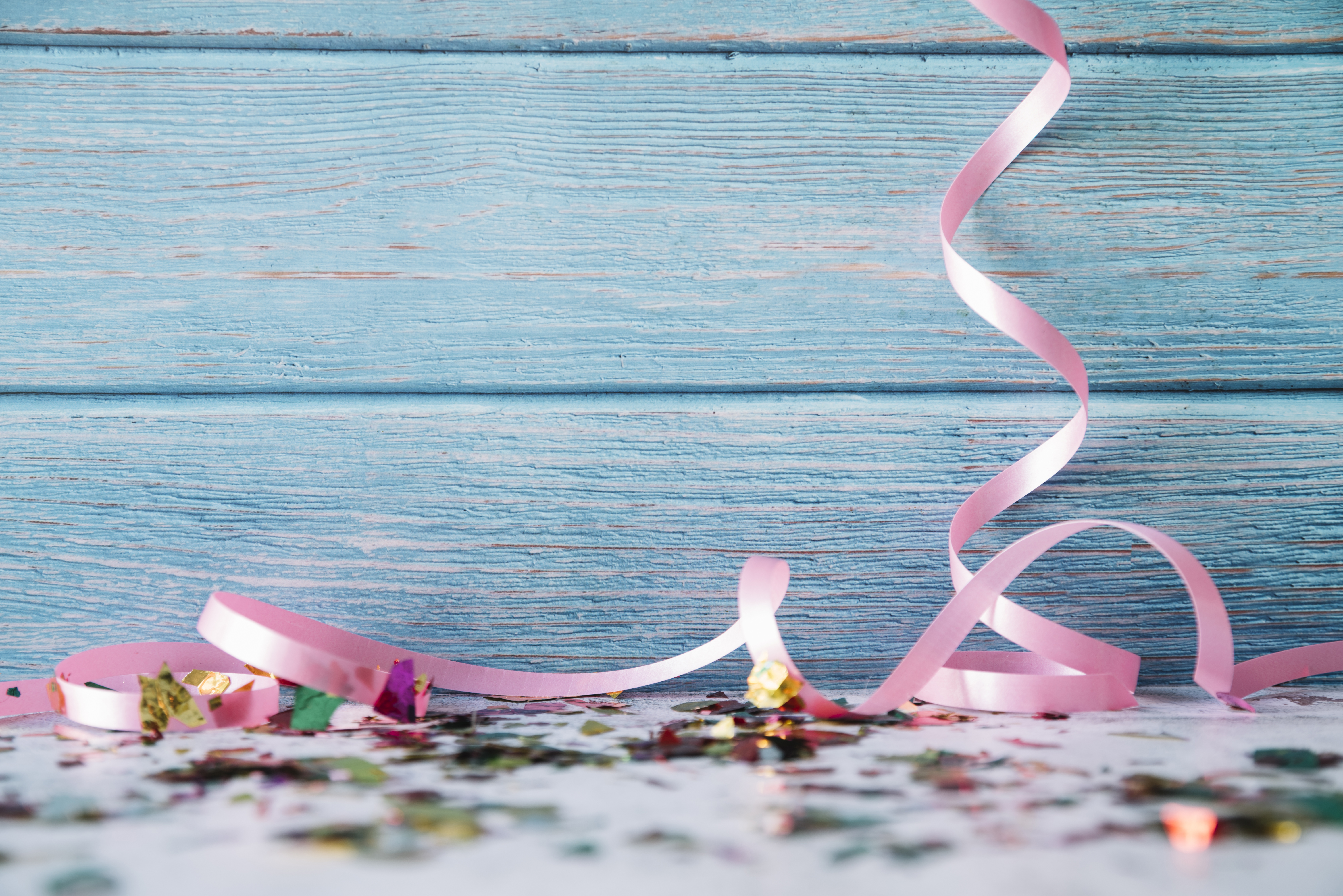 Confetti and pink ribbon in front of a blue wooden background.