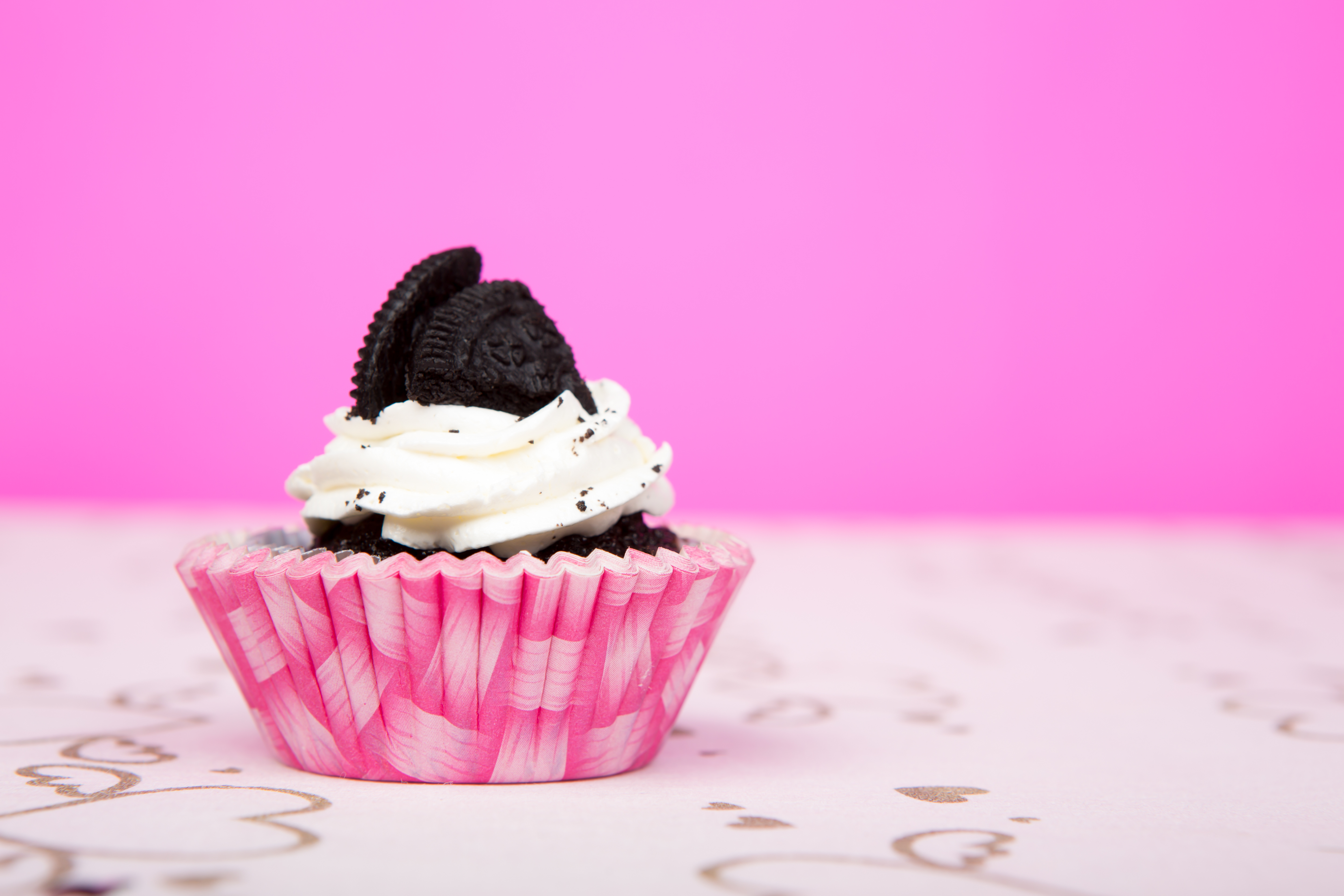 A small chocolate cupcake in a pink cupcake line in front of a pink background.