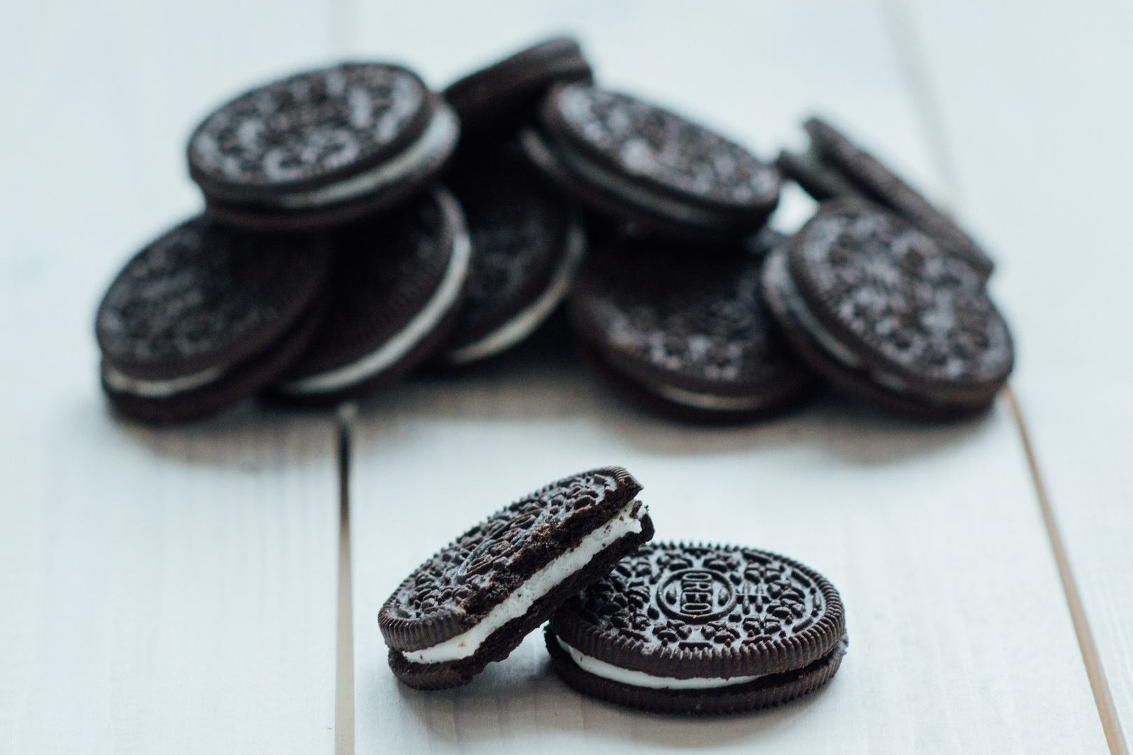 Two oreos in the front of the photo. One is missing a bite. A pile of oreos in the back of the photo, out of focus.