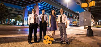 The musical group La Pompe standing on a street corner in Dallas at night.