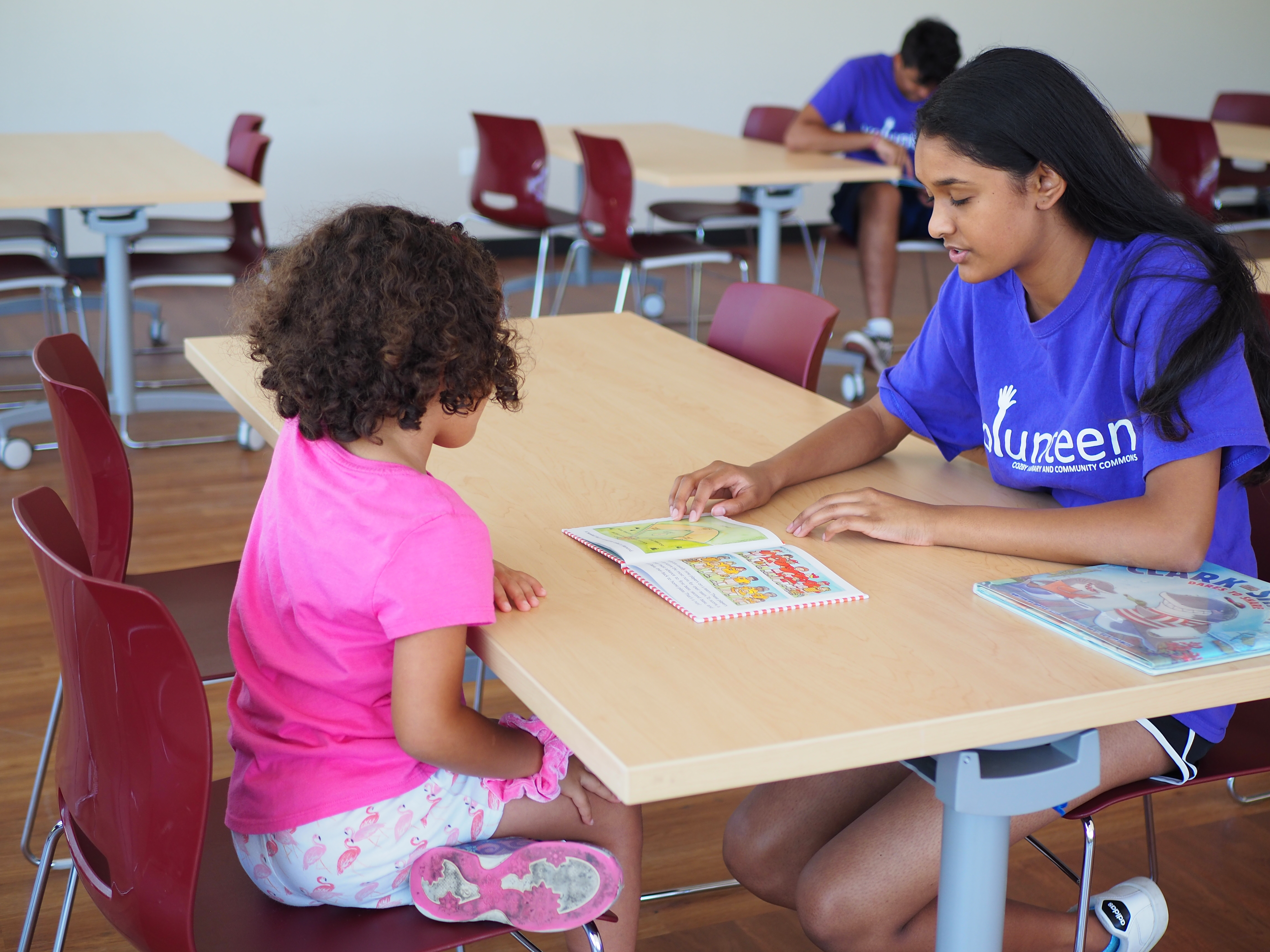 A child reading to a teen at a table.