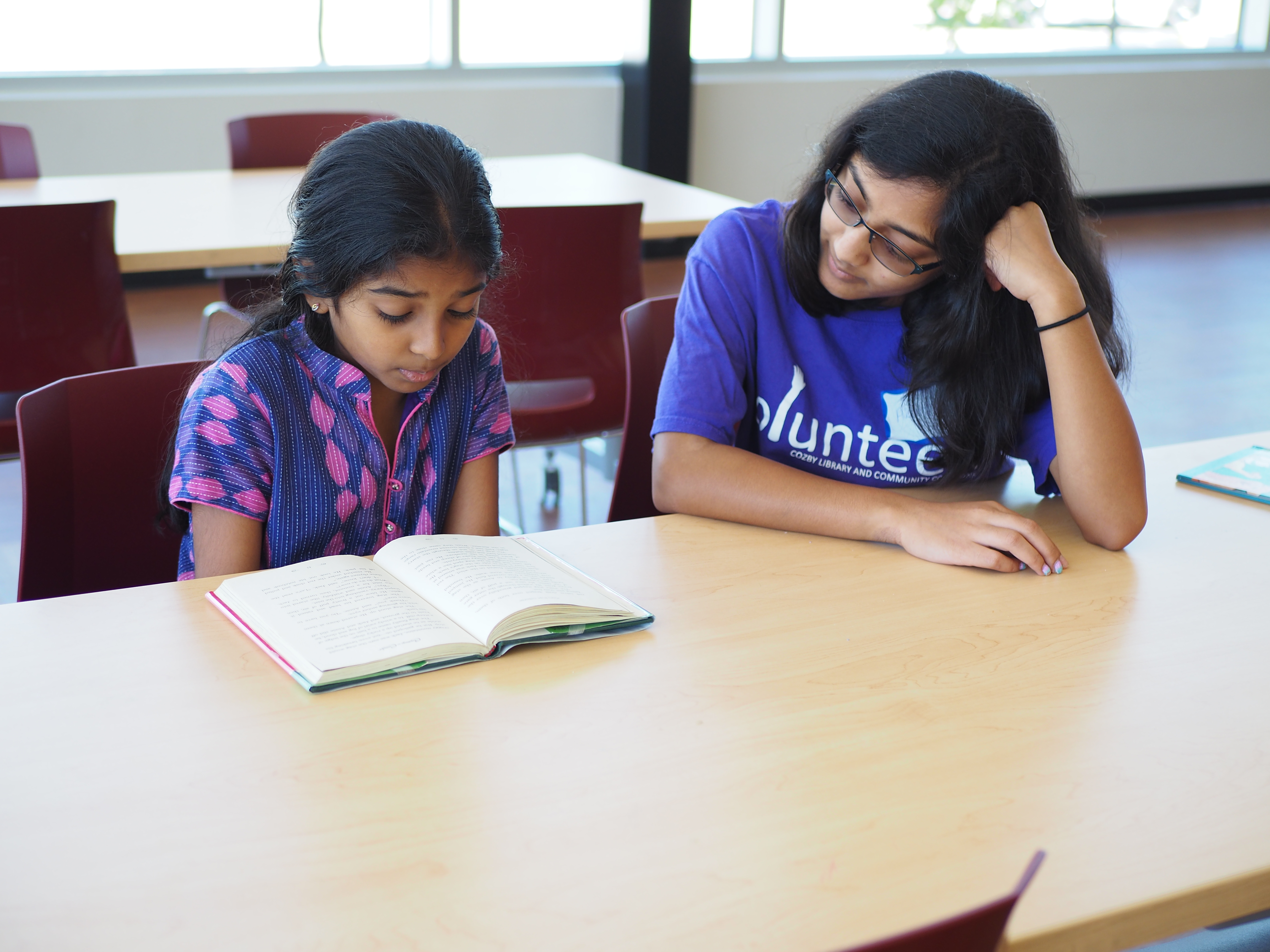 Elementary age kid reading to a teen at a table.