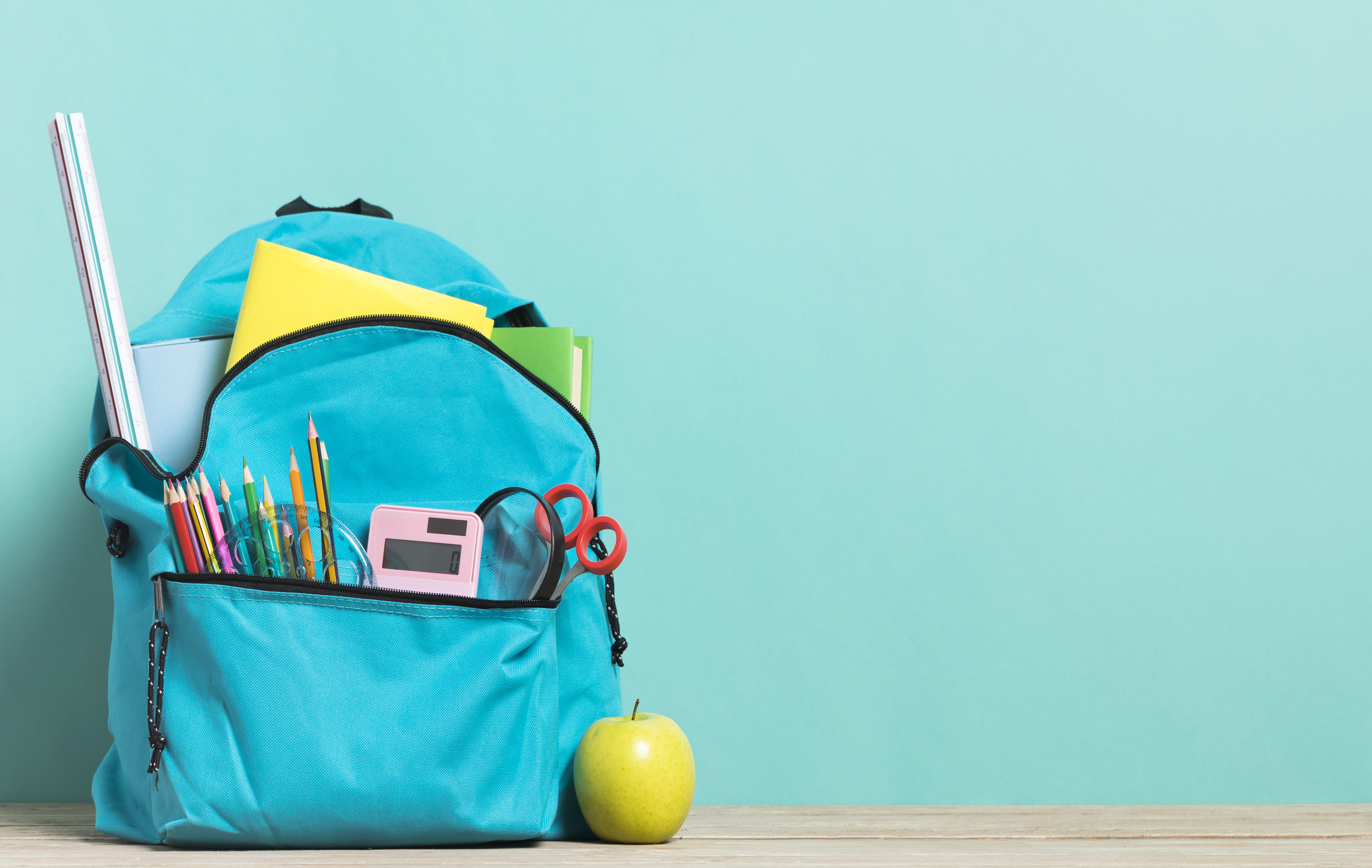 Blue backpack on a seafoam green background. Various school supplies sticking out of pockets.