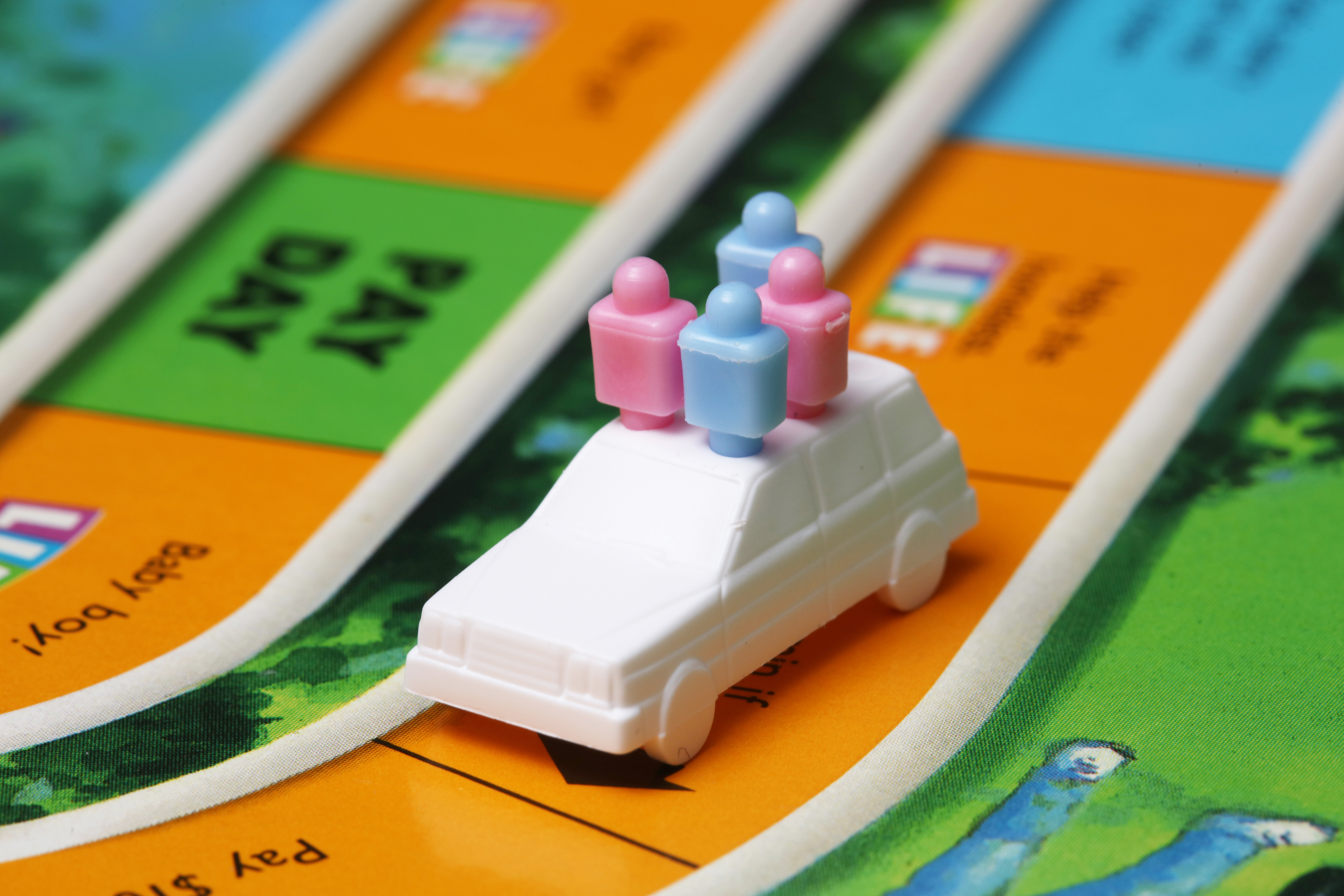 Close up photo of the board game Life. White plastic car with plastic peg people on the boardgame.
