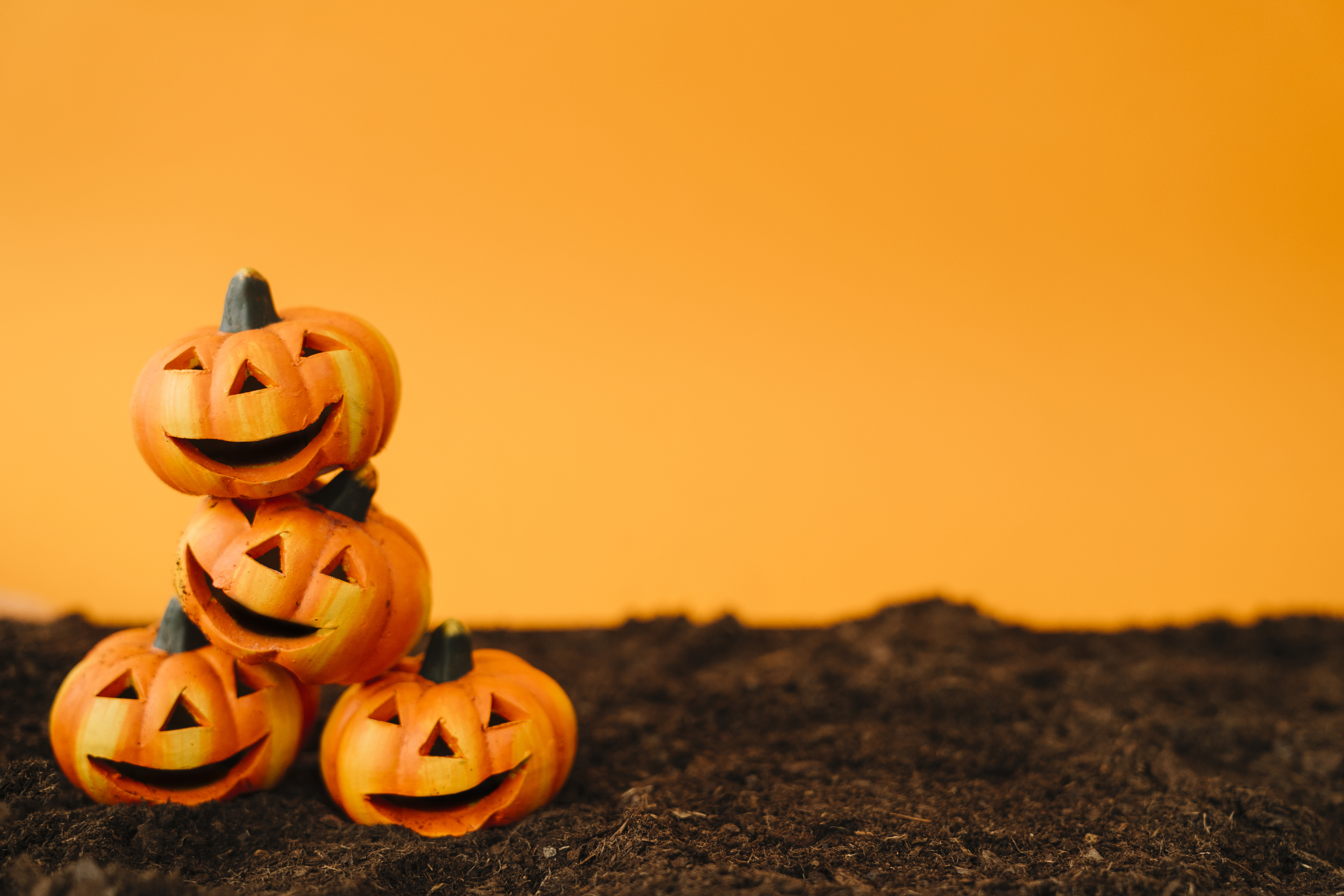 Stacked jack-o-lanterns sitting on the ground in front of an orange background.