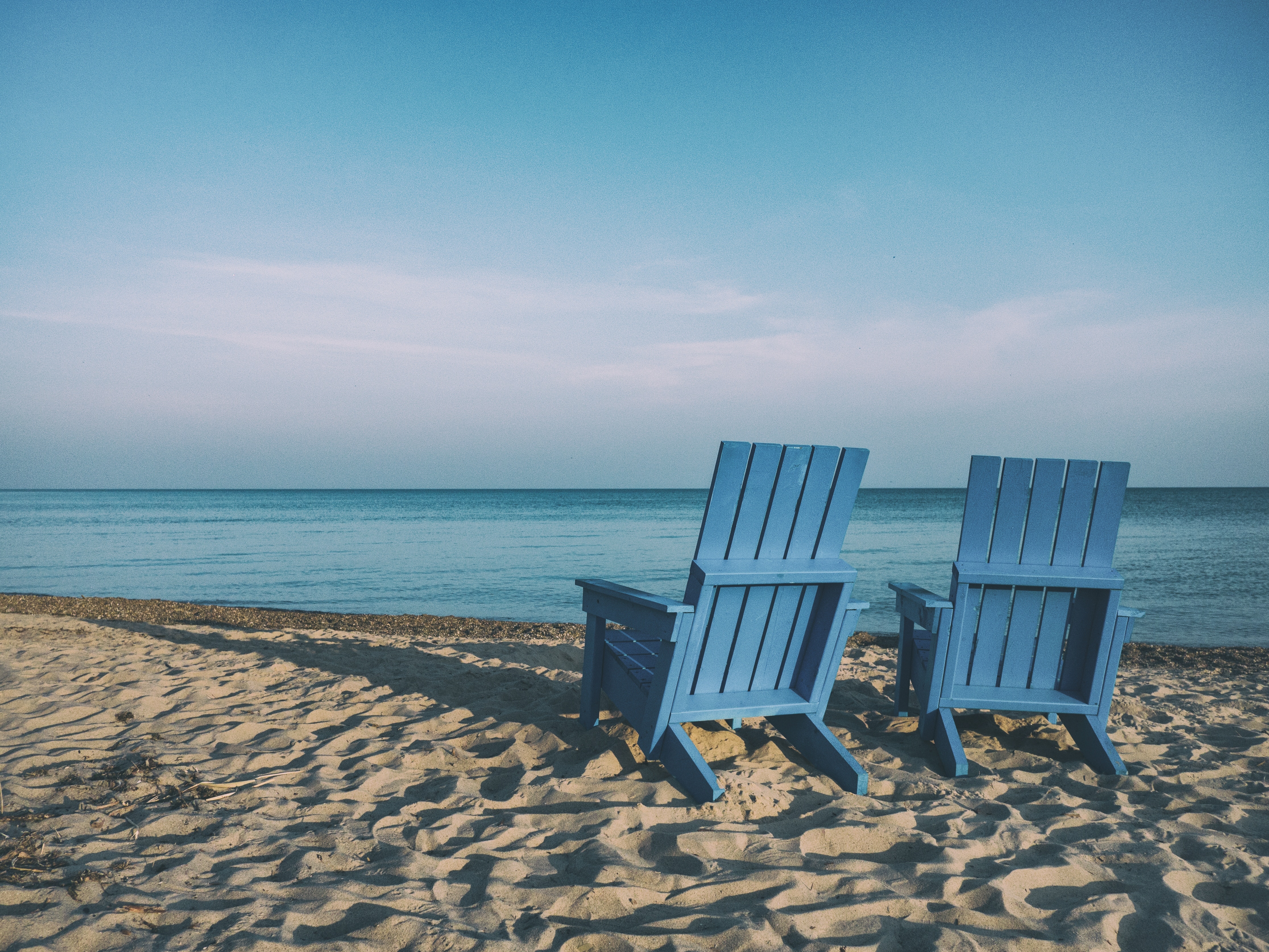 Two blue beach chairs sitting on the sand in front of the ocean.