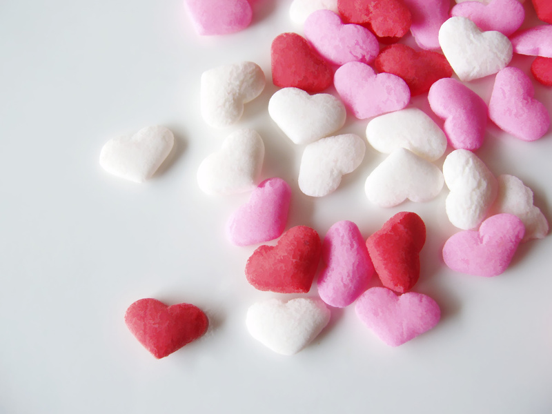 Red, white, and pink candy hearts scattered on a white table.