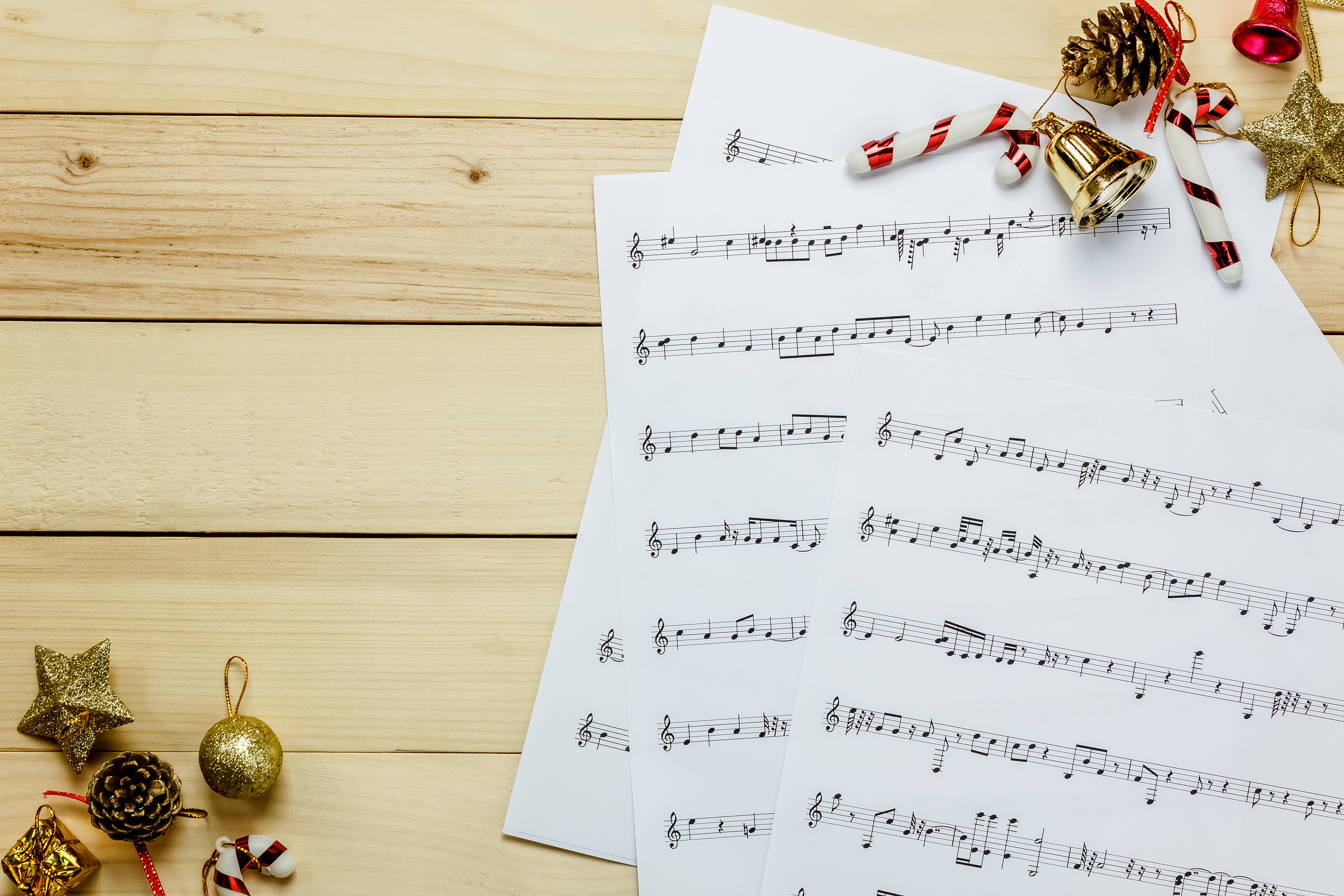 Sheet music on a wooden background with Christmas bells and ornaments around the border.
