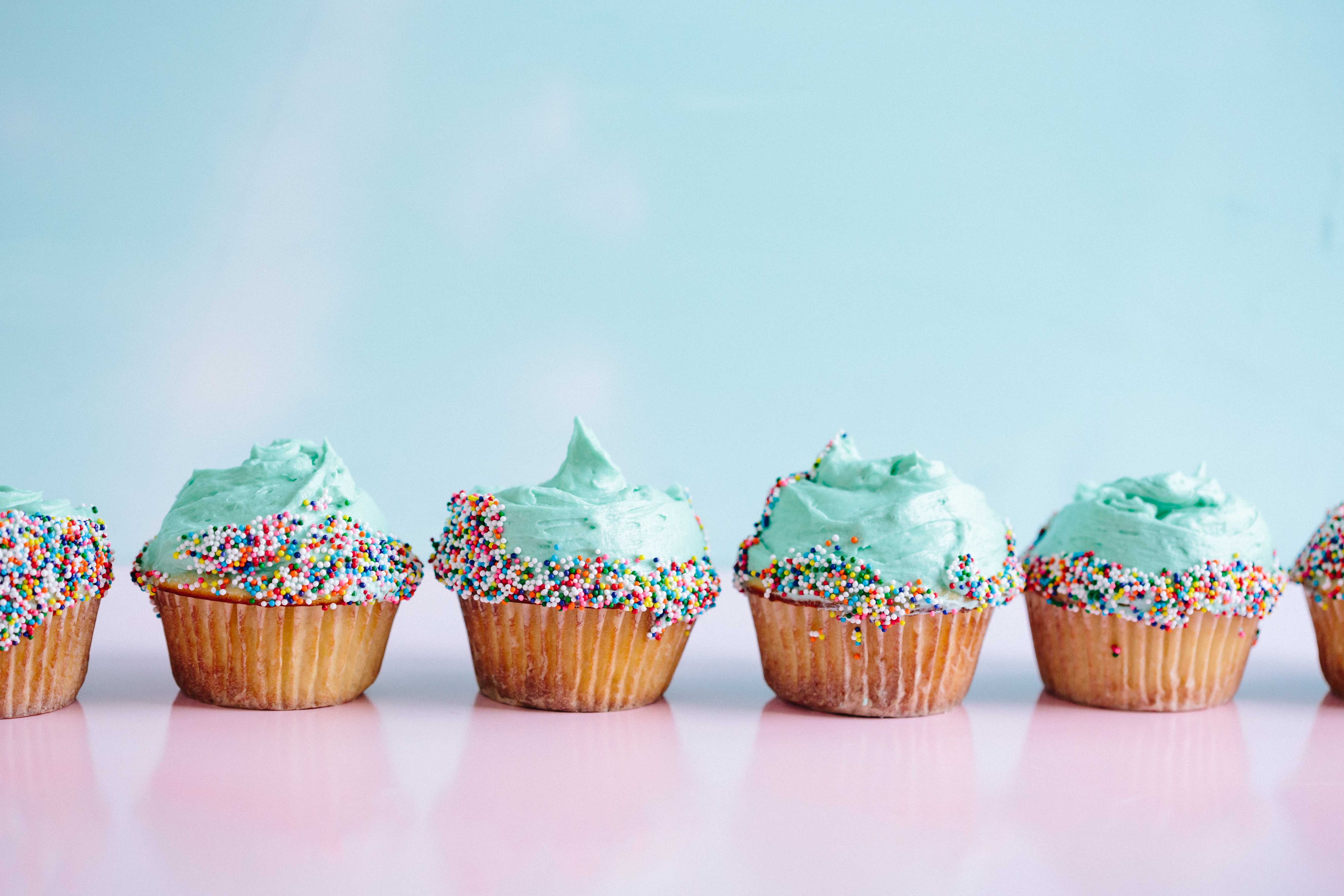 Cupcakes in a row with blue frosting and colorful sprinkles on a blue background.