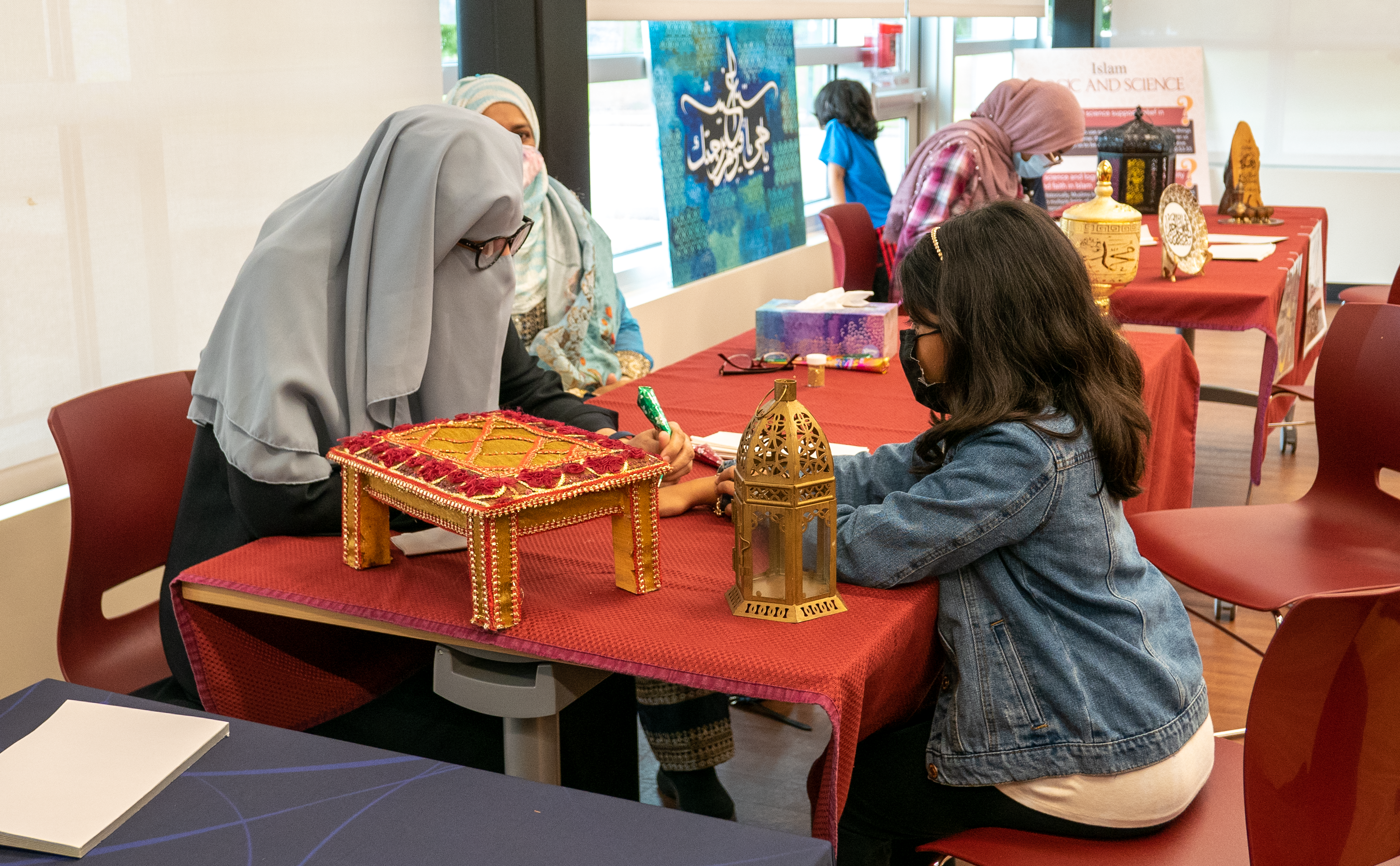 Woman wearing niqab sitting at table putting henna on a young girl. 