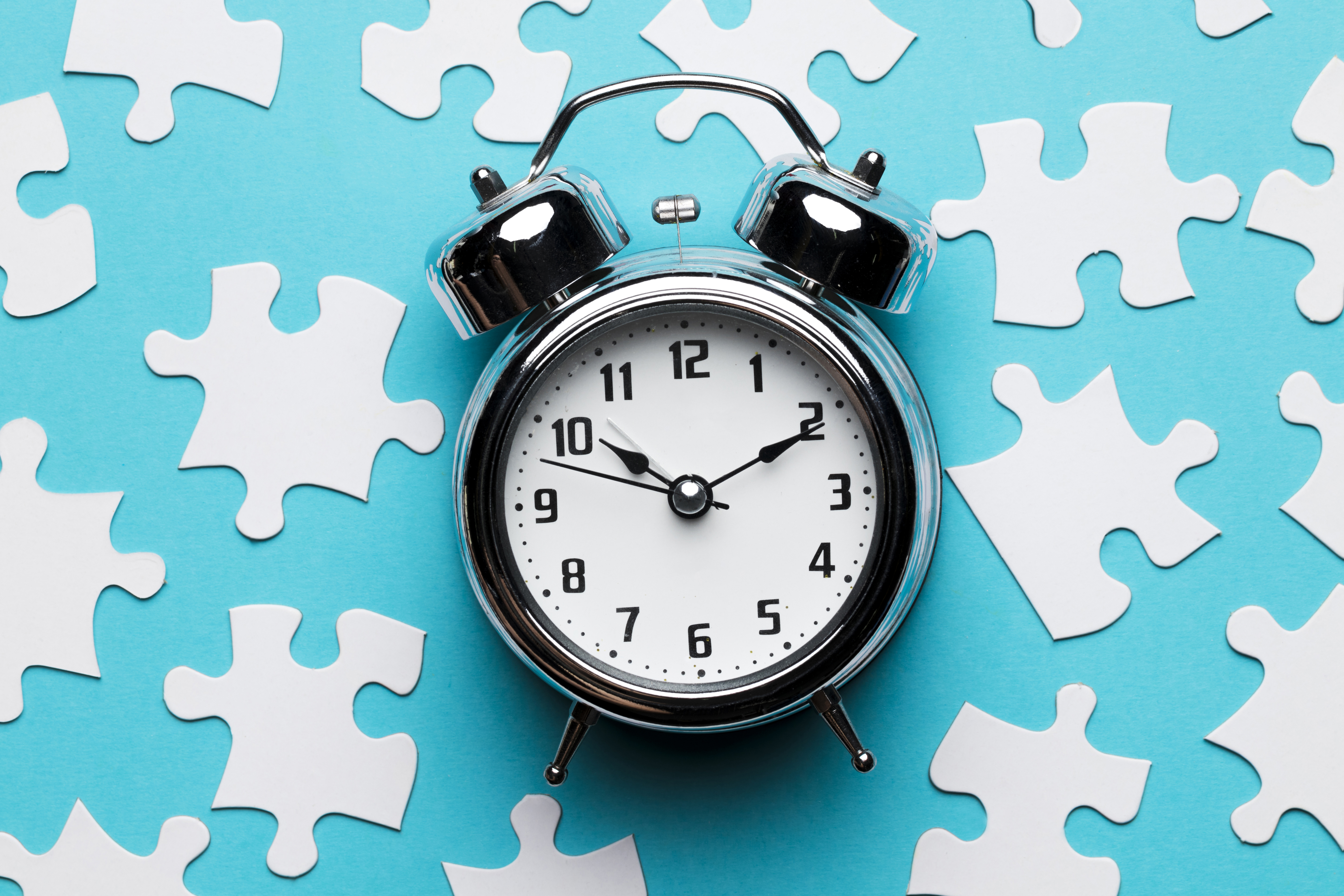Alarm clock on blue background with scattered white puzzle pieces.