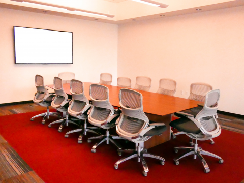 Conference room with long rectangular conference table, chairs, and mounted screen