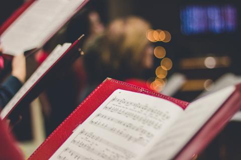 Close up of sheet music in a red book held by a member in a choir. 