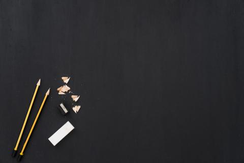 Two gold pencils with pencil shavings and a white eraser on a black background.