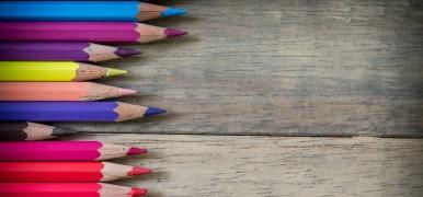 Colored pencils lined up on the left hand side on a wooden background.