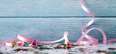 Confetti and pink ribbon in front of a blue wooden background.