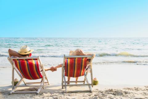 A couple in chairs on the beach facing the ocean.