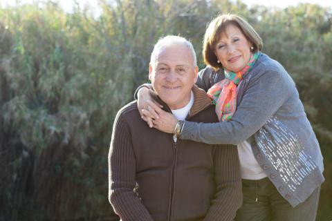 Older woman with her arms around the neck of an older man smiling at the camera.