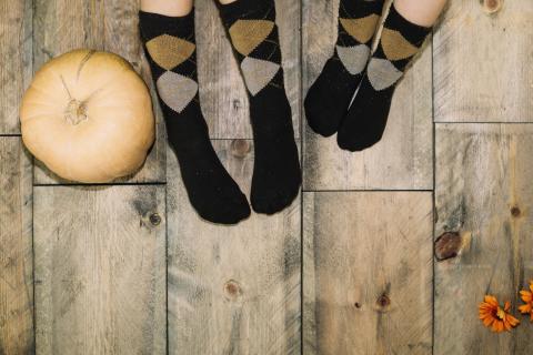 Photo of two pairs of feet in black argyle socks on a wooden floor next to a white pumpkin. 