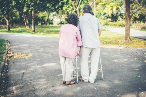 Elderly couple walking outside with a walker.