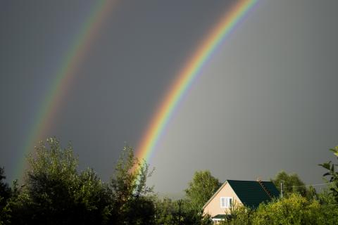 Two rainbows in a stormy sky over a farmhouse.