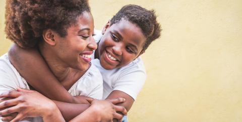 Mother smiling with son hugging her from behind smiling.