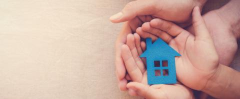 Adult and child hands holding a paper house.