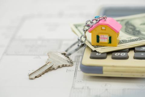 A house key on top of a calculator and dollar bills