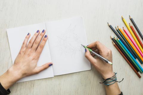 Overhead view of human's hand sketching on white drawing book