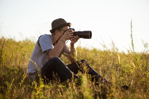 Young male photographer sitting in a field taking a photo
