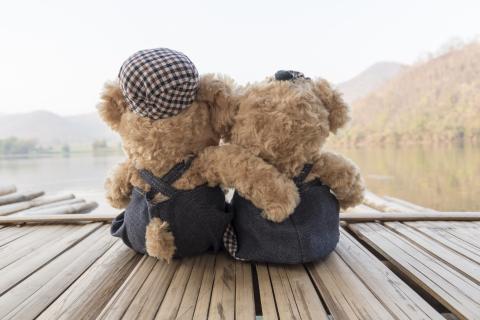 Teddy bears sitting on dock by water.