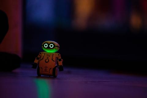 Robot with glowing green light and dark background.