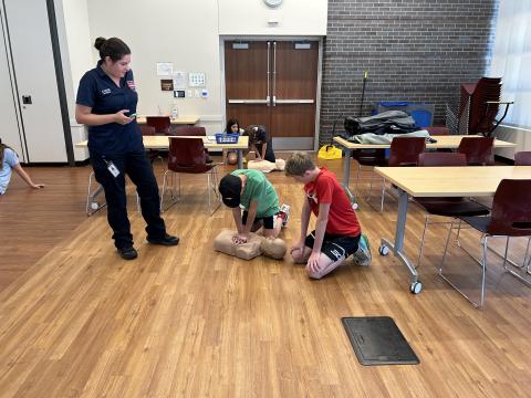 Two teen boys practicing CPR on a dummy with the instructor standing next to them.