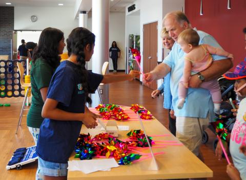 Teens handing a pinwheel to a man and child.