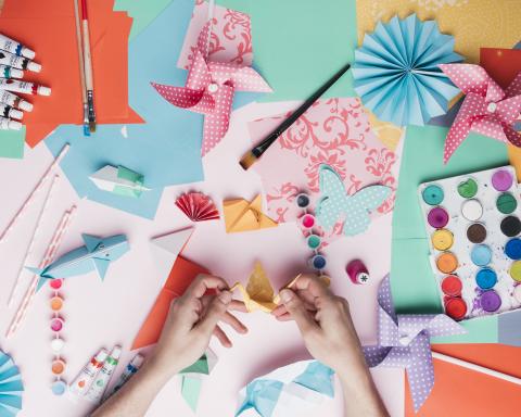 Various craft supplies scattered on table with hands working on crafts.