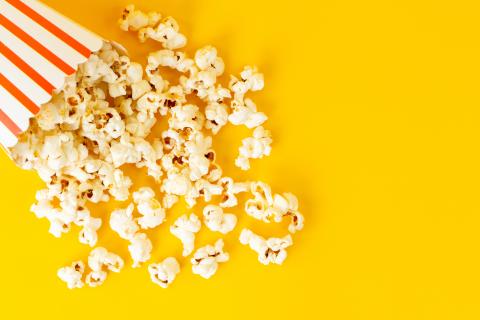 Tipped over red and white popcorn bucket with popcorn pouring out.