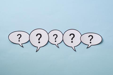 Paper speech bubbles with question marks inside them on a blue background.