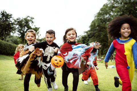 Kids running in grass in Halloween costumes.