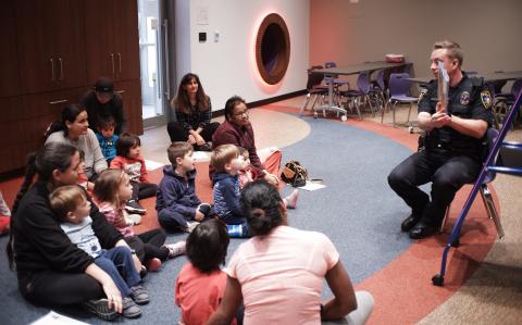 Police officer reading a story to families sitting on the floor.