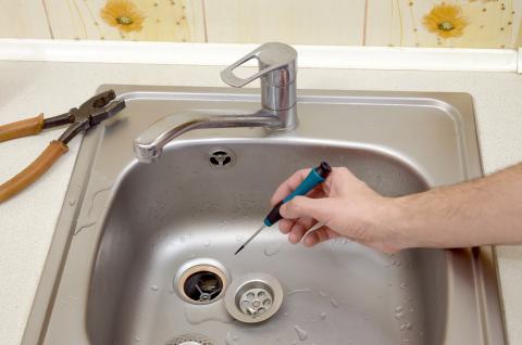 Hand holding a tool fixing a sink drain with pliers off to the side