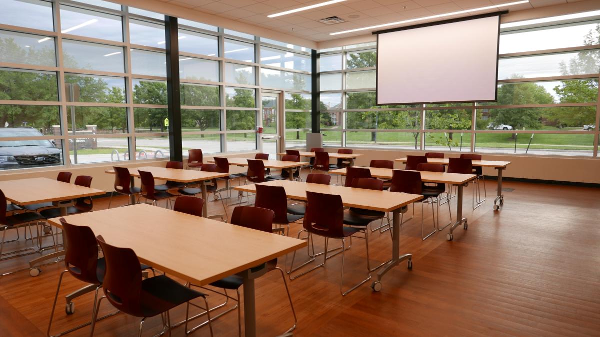 Meeting Room A with 8 tables, chairs, and a large white screen at front of room