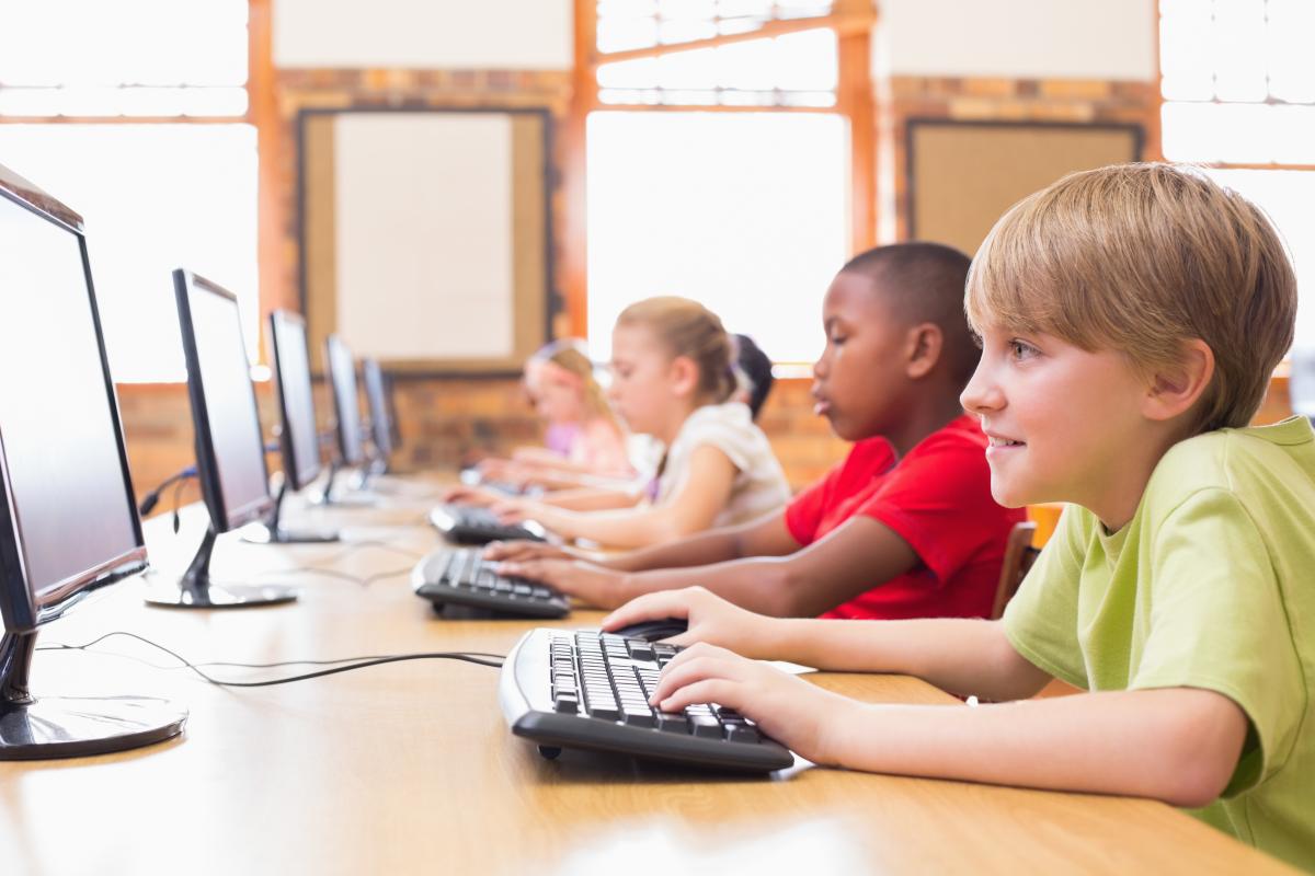 Several kids sitting at a long table using computers. 