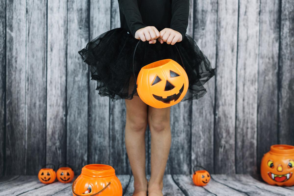 Image of a girl from the waist down wearing a black shirt and black tutu holding an orange jackolantern basket.