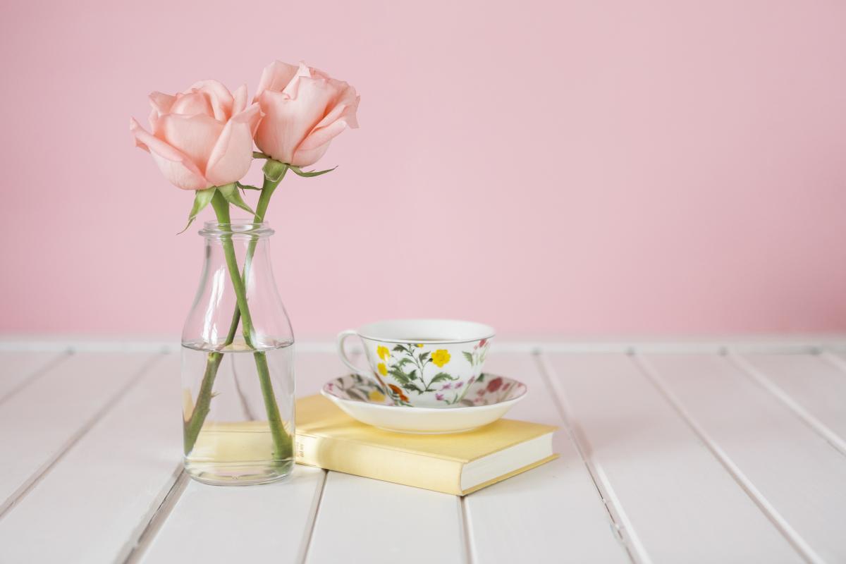 Teacup on top of a book with a vase with pink flowers. 