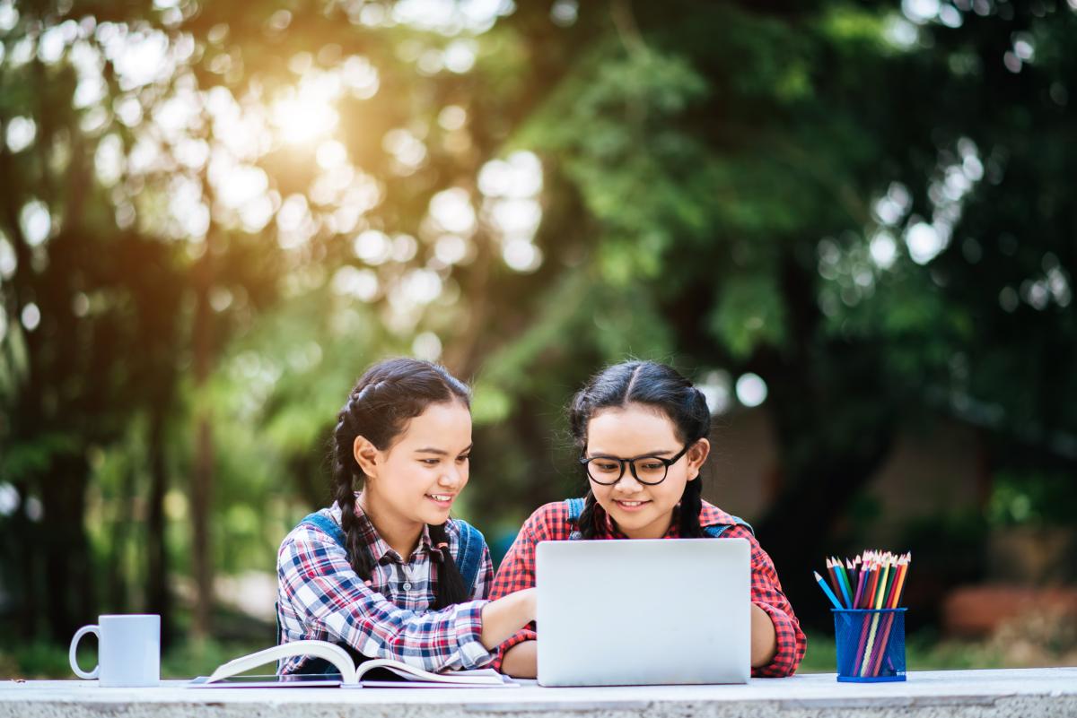 Two girls sitting at a table outside working on a laptop.